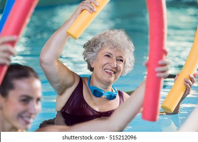 Smiling senior woman doing aqua fitness with swim noodles. Happy mature healthy woman taking fitness classes in aqua aerobics. Healthy old woman holding swim noodles doing aqua gym with young trainer. - Powered by Shutterstock