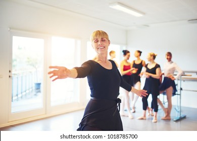 Smiling Senior Woman Doing Ballet Dancing In A Dance Studio With A Group Of Friends In The Background