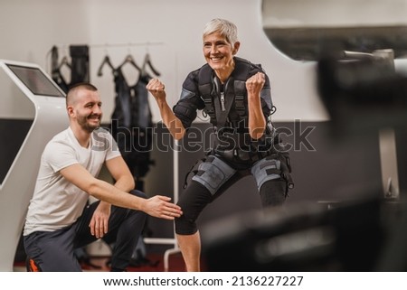Smiling senior woman is doing EMS working out with personal trainer in the gym.