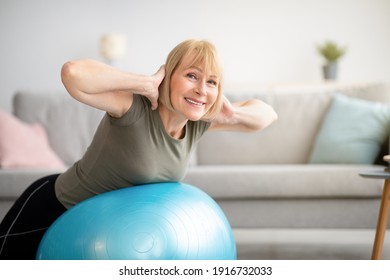 Smiling senior woman doing exercises with fitness ball at home, space for text. Mature Caucasian lady working out her back muscles, training with sports equipment during coronavirus lockdown - Powered by Shutterstock