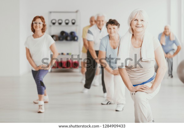 Smiling senior woman exercising with group of\
active seniors in fitness\
center