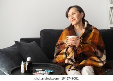 Smiling senior woman feels relieved, recovering after viral disease. An elderly female covered blanket sits on the couch, drinks hot and feels better. Healthcare concept - Powered by Shutterstock