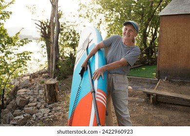 a smiling senior woman with gray hair holding sup board on the seashore at sunset. copy space. Slow life. Enjoying the little things. spends time in nature in summer - Powered by Shutterstock