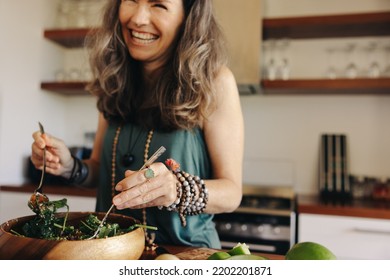 Smiling senior woman having a delicious buddha bowl in her kitchen. Excited woman serving herself some healthy vegan food at home. Mature woman taking care of her aging body with a plant-based diet.