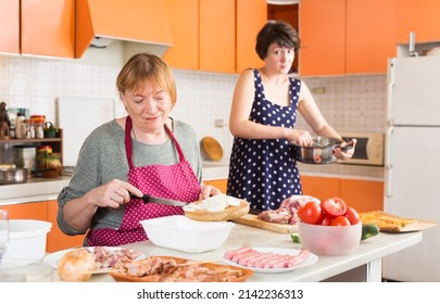 Smiling senior woman and her daughter-in-law preparing dinner for family in comfortable home kitchen