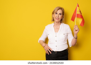 Smiling senior woman holding spanish flag standing isolated over yellow background. - Powered by Shutterstock