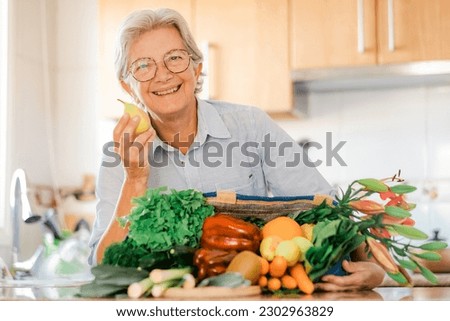 Smiling senior woman in home kitchen with a bag full of vegetables and fruit on the table, grocery purchases for vegan or vegetarian people, healthy eating concept