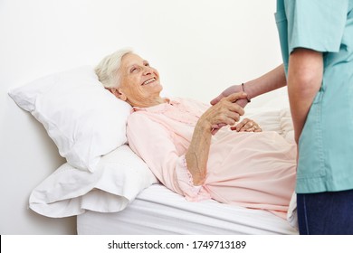 Smiling Senior Woman Lies In Bed In Hospice And Shakes Hands With A Nurse