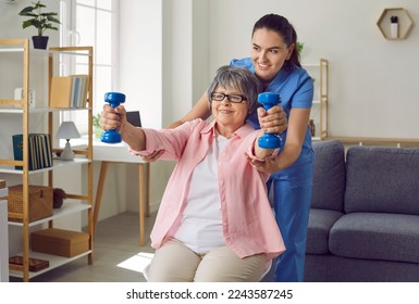 Smiling senior woman lifting dumbbells, therapist assisting her. Cheerful female nurse helping elderly patient to do physical exercise at home. Disabled, elderly people rehabilitation and support - Powered by Shutterstock