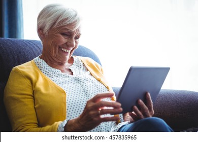 Smiling senior woman looking and laughing at her digital tablet in a sofa - Powered by Shutterstock