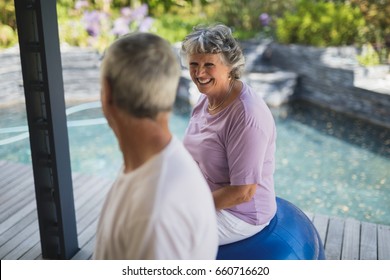 Smiling senior woman looking at man while sitting on exercise ball at porch - Powered by Shutterstock