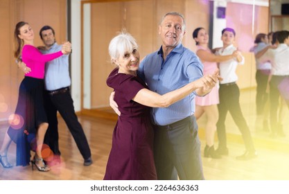 Smiling senior woman and man dancing slow ballroom dance during group class in choreography studio - Powered by Shutterstock