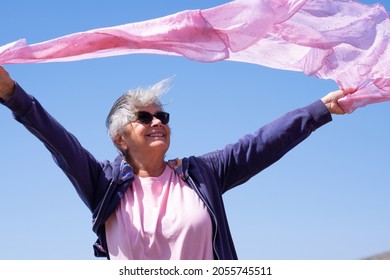 Smiling Senior Woman On A Windy Day Leaves Her Scarf Waving. Elderly Person Enjoys The Vacation And Retirement