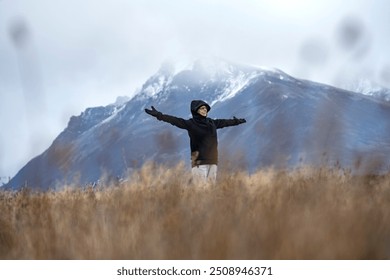 Smiling senior woman open her arms and embrace nature in the middle of the field in front of a mountain. - Powered by Shutterstock