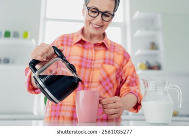 Smiling senior woman pours coffee in kitchen, enjoying a relaxing morning - Powered by Shutterstock