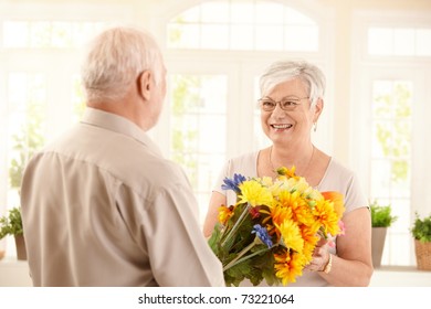 Smiling Senior Woman Receiving Bouquet Of Flowers From Elderly Man.?