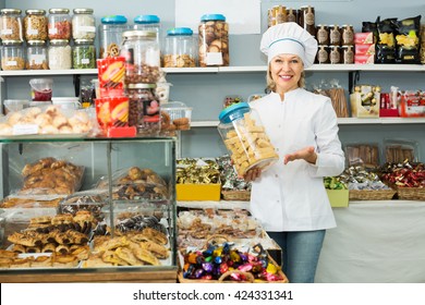 Smiling Senior Woman Selling Nuts And Pastry In Shop