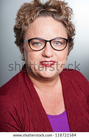 Smiling senior woman with short curly hair. Wearing glasses. Studio shot.