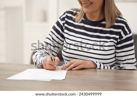 Smiling senior woman signing Last Will and Testament at wooden table indoors, closeup