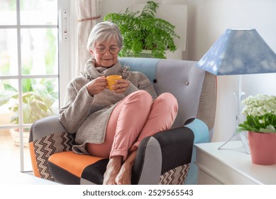 Smiling senior woman sitting on armchair and holding coffee cup. Caucasian female relaxing in cozy living room and having coffee. - Powered by Shutterstock