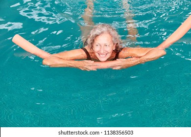 Smiling senior woman in the swimming pool is doing aqua fitness with buoyancy aid - Shutterstock ID 1138356503