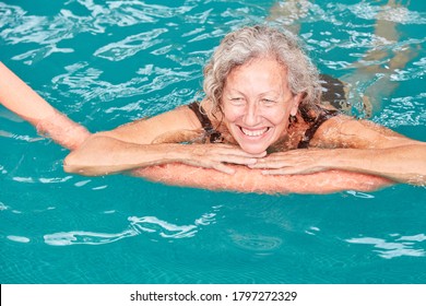 Smiling senior woman in swimming pool at aqua fitness with a swimming noodle