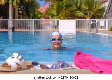 Smiling senior woman swims in the outdoor swimming pool  wearing swimming cap and goggles. Happy elderly lady enjoying healthy lifestyle and summer holidays