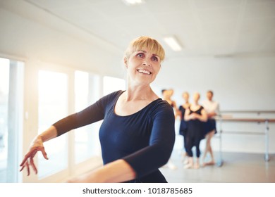 Smiling Senior Woman Taking Ballet Lessons In A Dance Studio With A Group Of Friends In The Background