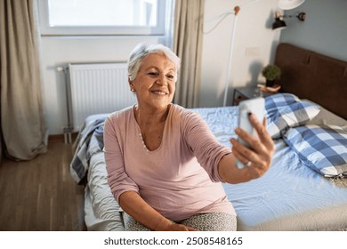 Smiling senior woman taking selfie in bedroom at home - Powered by Shutterstock