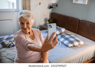 Smiling senior woman taking selfie in bedroom at home - Powered by Shutterstock