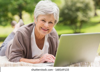 Smiling Senior Woman Using Laptop While Lying At The Park