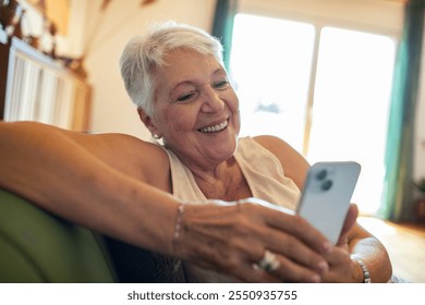 Smiling senior woman using smartphone on couch at home - Powered by Shutterstock