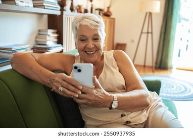 Smiling senior woman using smartphone on couch at home - Powered by Shutterstock