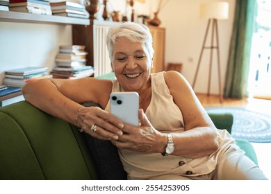 Smiling senior woman using smartphone on couch at home - Powered by Shutterstock