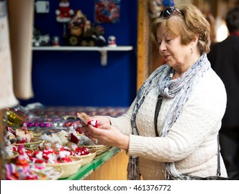 Smiling senior woman walking on the Christmas Fair and chosen decoration