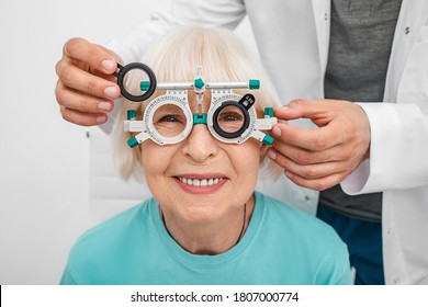 Smiling senior woman wearing optometrist trial frame at ophthalmology clinic. Ophthalmologist helping select glasses for treatment of vision. Eye check-up - Powered by Shutterstock