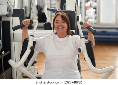 Smiling Senior Woman Working Out At Gym. Healthy Elderly Woman Exercising Using Chest Press Machine At Fitness Club. Active Way Of Life.