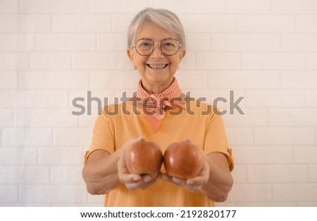Smiling senior woman in yellow t-shirt on a white background holding two red apples fruit in her hands looking at camera - healthy eating concept