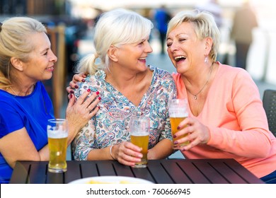 Smiling senior women having a beer in a pub outdoor
