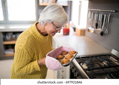 Smiling senior women holding freshly baked muffins wearing oven gloves - Powered by Shutterstock