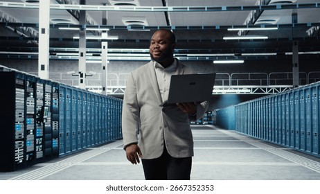Smiling server room engineer performing maintenance on server racks using software on laptop. Happy data center IT professional upgrading blade server components using notebook, camera A