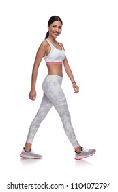 Smiling Sexy Woman Walking To Side In Gym Clothes On White Background. She Is Wearing A Pair Of White Leggings And A White Top