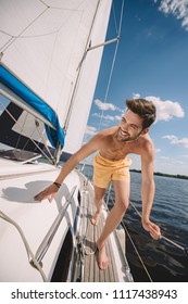 Smiling Shirtless Man In Swim Trunks Running On Yacht 