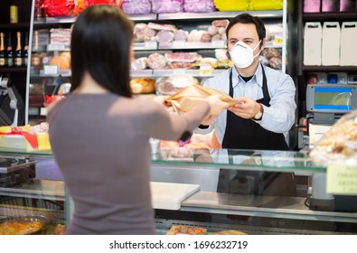 Smiling shopkeeper serving a customer while wearing a mask, coronavirus pandemic concept - Powered by Shutterstock
