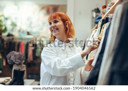 Smiling shopper in clothing store. Woman looking at clothes hanging on rack in fashion store.