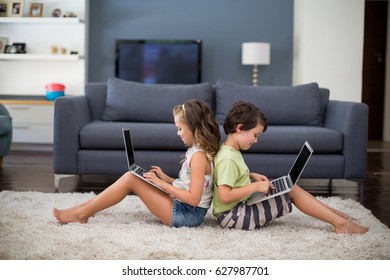 Smiling siblings sitting back to back and using laptop in living room at home - Powered by Shutterstock