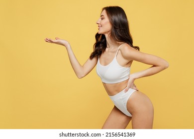 Smiling Side View Lovely Attractive Young Brunette Woman 20s In White Underwear With Perfect Fit Body Stand Posing Hold Show Empty Arm With Workspace Area Isolated On Plain Yellow Background Studio