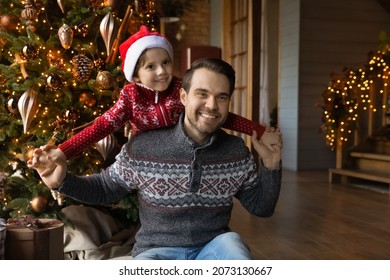 Smiling sincere young father playing plane with adorable small preschool kid son, spending relaxed holiday family time together near decorated festive evergreen Christmas tree in designed living room.