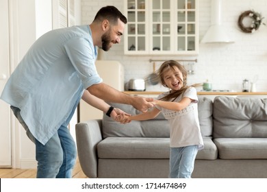 Smiling single dad enjoying funny family activity with laughing little preschool daughter in modern studio living room. Happy small child girl dancing to favorite pop music with joyful father indoors. - Powered by Shutterstock