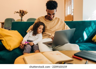 Smiling Single Father Showing His Daughter An Educational Video On A Laptop. Loving Single Dad Homeschooling His Young Daughter. Happy Father And Daughter Sitting On A Couch At Home.